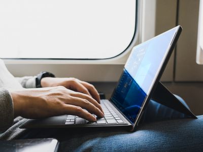 A man sitting on a train with a Microsoft Surface Pro laptop on his lap running Windows 11 that looks like Windows 10.