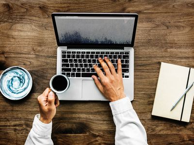 Person browsing internet on laptop with coffee cup in hand