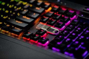 A computer keyboard showing multi-colored backlights and a hardware security key.