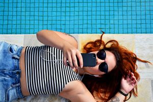 Someone laying next to a pool listening to streaming music on a smartphone.