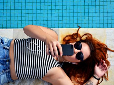 Someone laying next to a pool listening to streaming music on a smartphone.