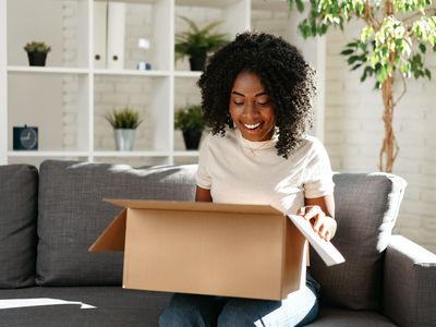 Person sitting on couch unpacking cardboard box.