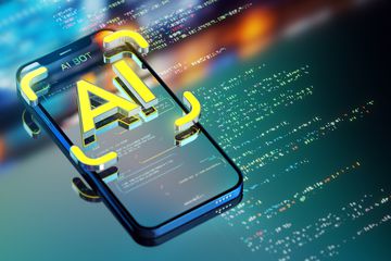 A yellow AI icon on top of a smartphone sitting on a screen, both with code displayed. 