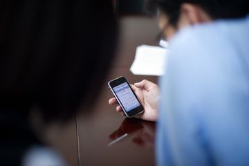 Someone watching over a shoulder as a person uses their cellphone.