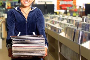 A woman holding a stack of vinyl records while standing inside a music store.