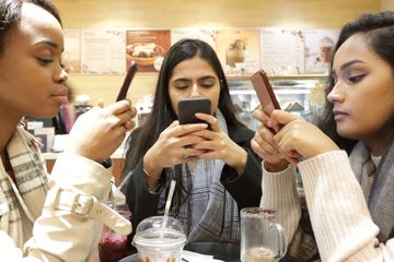 Three young woman on phones in cafe