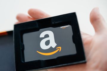 A hand holds an Amazon gift card in a black case